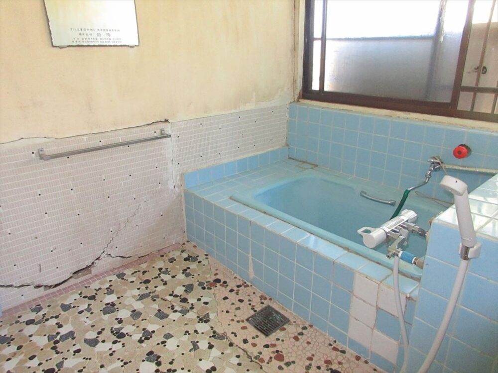 岩手県遠野市の物件の風呂。バスルームも壁のひび割れやタイルのはがれが見受けられるので、大幅な改修が必要だ。