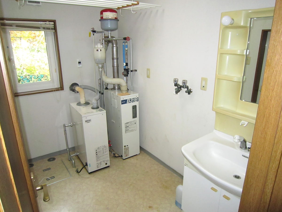 北海道弟子屈町の物件の脱衣所には給湯・床暖房用ボイラーが置かれています。洗面台の左側が洗濯機置場です。