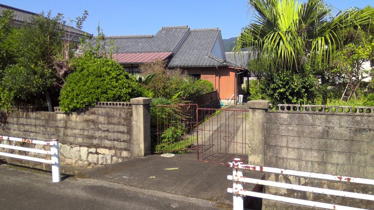 【写真】鹿児島県肝付町の100万円物件の外観。敷地は石垣で囲まれており、庭と畑のある広い敷地の邸宅です。