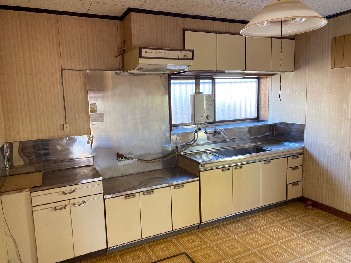 岩手県久慈市の物件のキッチンは、ガスコンロと調理家電を置くことができる広いスペースがとられています。収納スペースも多く、使い勝手がよさそうです。右手に勝手口があります。
