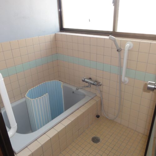 長崎県雲仙市の物件のピンクのタイルで清潔感のある浴室は、すぐに使用できる状態です。シャワーも装備されています。手すり付きなのも嬉しいポイントです。