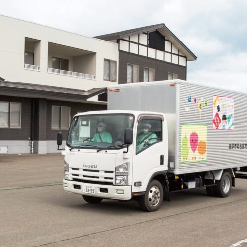 給食センターの入った“ぱすぽる”の建物の前から、できたての給食を積んだトラックが学校に向けて次々に走り出す（岩手県遠野市）