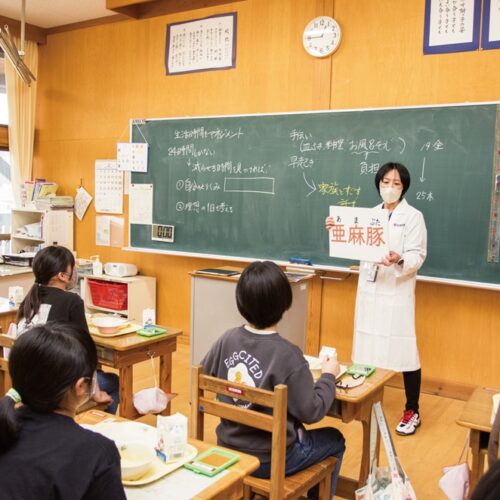 黒田さんは給食中の各教室を回る。食べ物を身近に感じてほしいと、亜麻豚が近くの農場で育てられていることや、給食センターでの調理のようすを説明（岩手県遠野市）