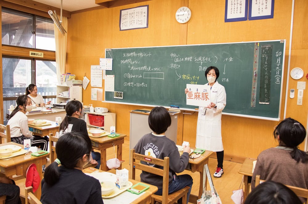 黒田さんは給食中の各教室を回る。食べ物を身近に感じてほしいと、亜麻豚が近くの農場で育てられていることや、給食センターでの調理のようすを説明（岩手県遠野市）