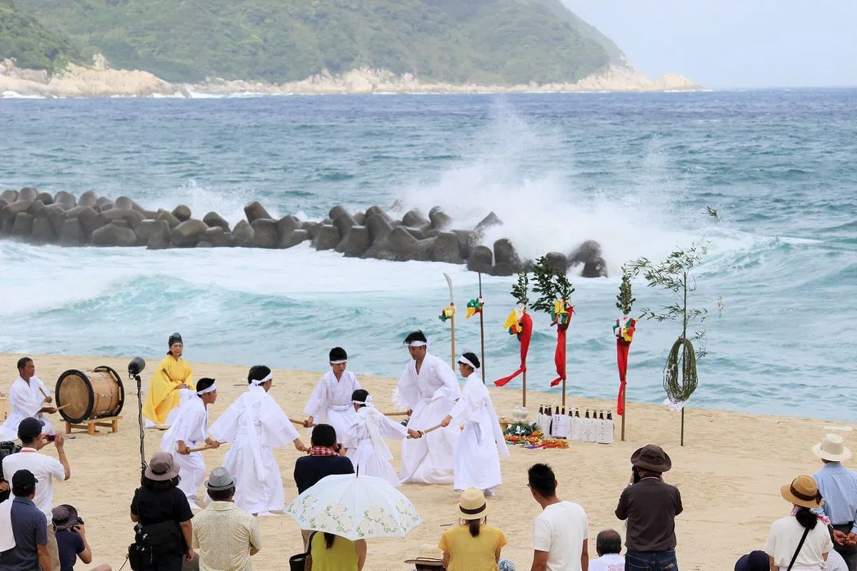 鹿児島県肝付町の岸良地区に伝わる伝統行事「岸良のナゴシドン」は、古くから人々の暮らしに根ざした夏越祭です。 平田神社を舞台に、地域住民が一体となって神楽を奉納し、一年の無病息災を祈願します。力強い太鼓の音と神楽の舞が、夏の暑さを吹き飛ばし、人々の心を清めます。白い砂浜と青々とした海、真っ赤な神面三体、白い衣装で神舞を奉納する舞手たちは、肝付町でしか見られない夏の風物詩です。