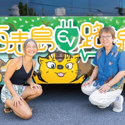 沖縄県の西表島へ移住した坂井さん。西表島交通のEVバスの前で