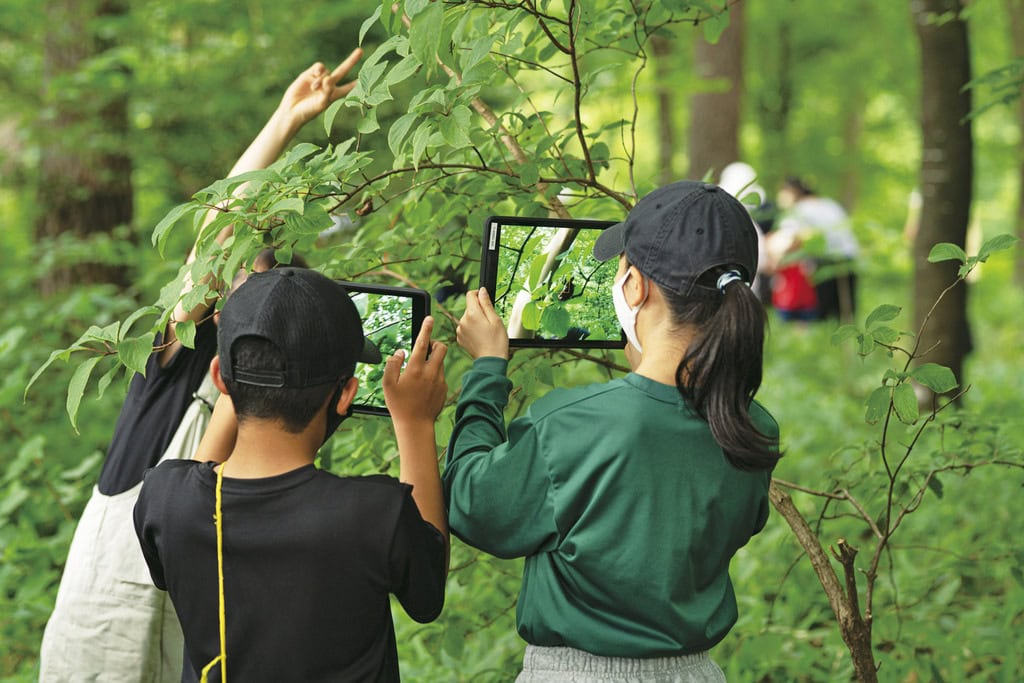 伊那西小学校では、校舎に隣接する森にタブレットを持ち出し、探究学習を行っている。森の中でもWi-Fi環境が整い、子どもたちは植物観察に夢中。