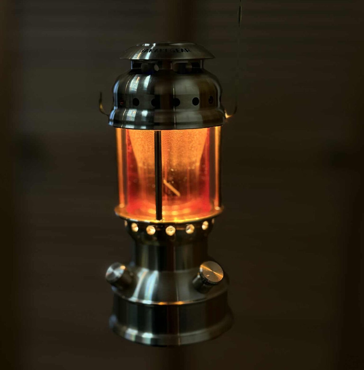 薄暗い室内で、オレンジ色の鮮やかな光を放つ真鍮製ランタン「まほろば」が吊り下げられている様子。